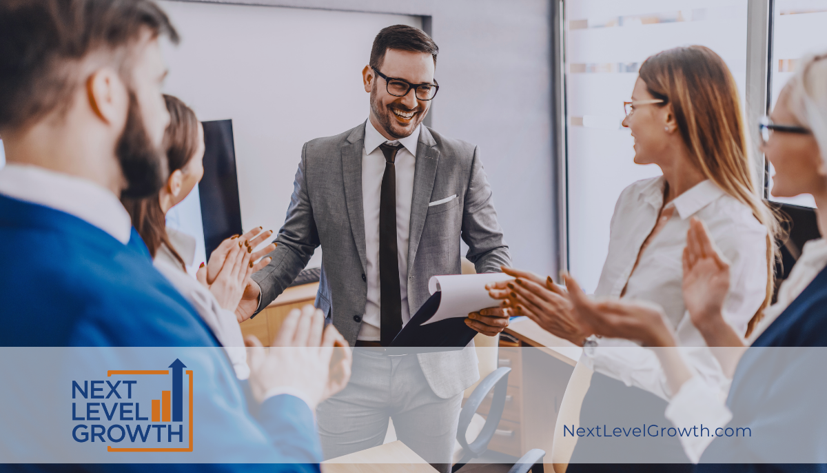 A man in a suit smiles while holding papers, standing with colleagues who are applauding in a modern office—celebrating success and fostering a high-performance culture. "Next Level Growth" logo and website appear on the image.