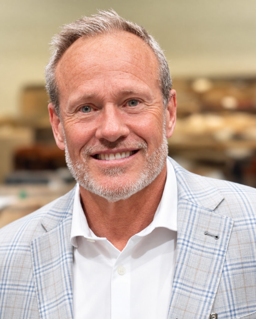 Dan Manson, a middle-aged man with short gray hair and a beard, wearing a plaid suit jacket and white shirt, smiles at the camera in an indoor setting.